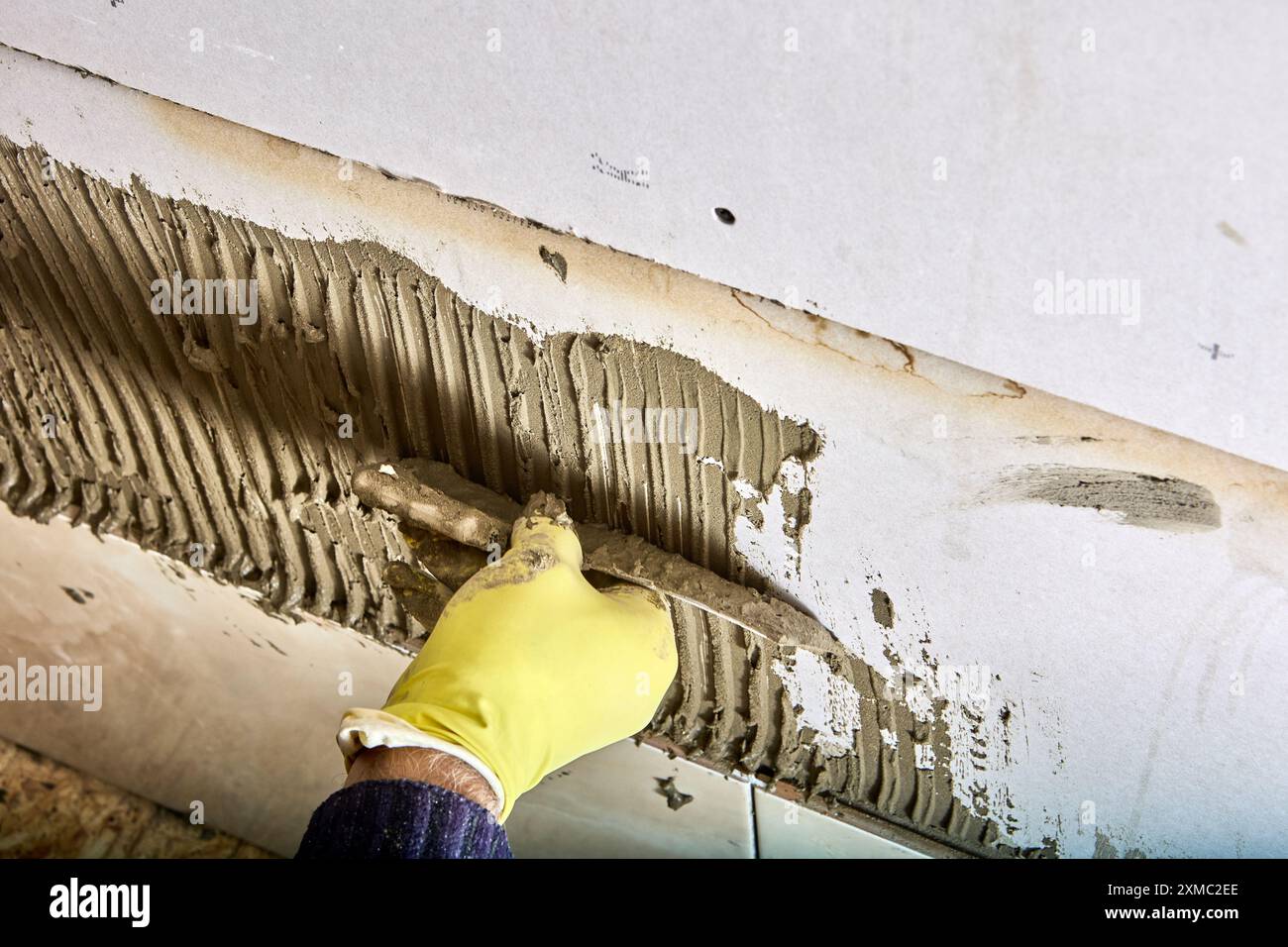 Le carreleur Builder applique du mortier de ciment adhésif sur le mur à l'aide d'une truelle à peigne. Banque D'Images