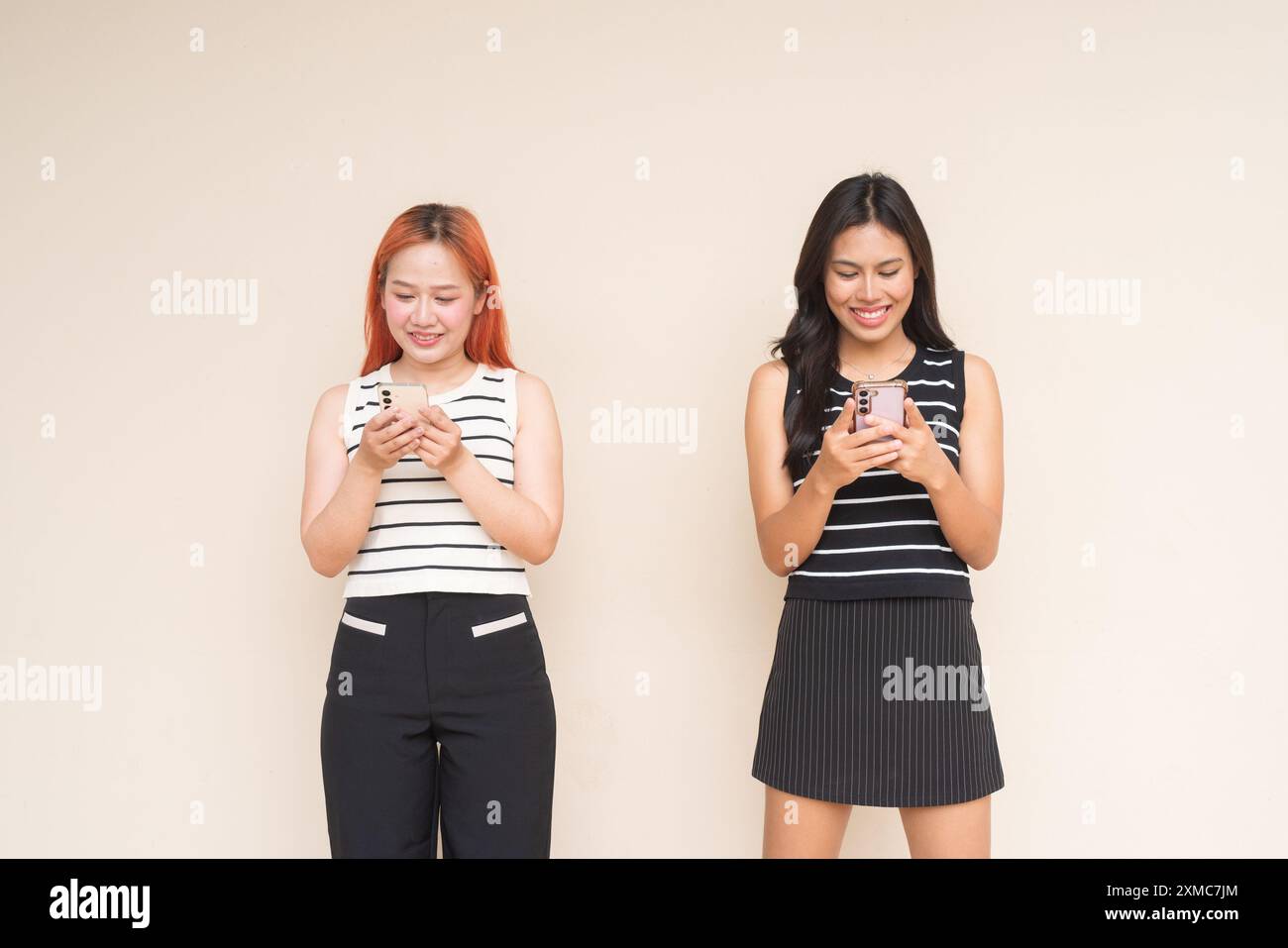 Portrait de deux femmes asiatiques heureuses souriant à l'extérieur en utilisant le téléphone portable et SMS Banque D'Images