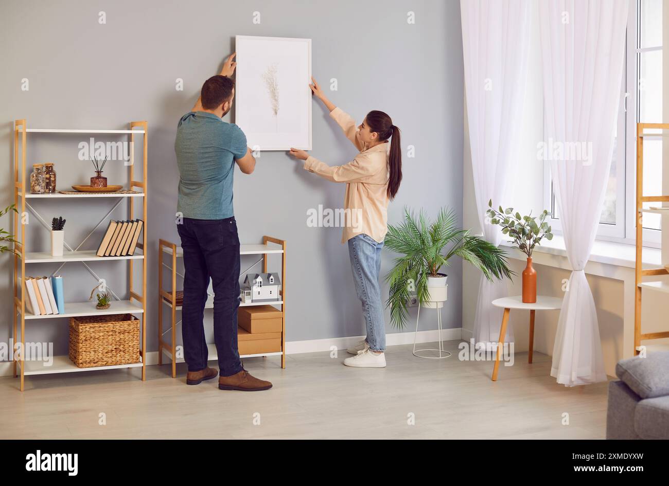 Jeune couple décorant leur maison et accrochant l'image sur le mur dans le salon Banque D'Images