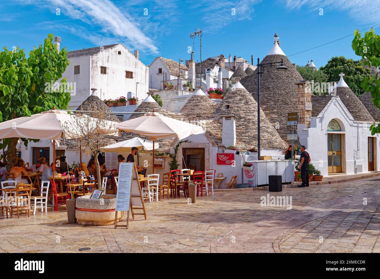 Trulli blanchis à la chaux, maisons rondes aux toits en pierre, dans la ville italienne méridionale d'Alberobello. Au premier plan, un restaurant sur la via Monte Santo. Banque D'Images