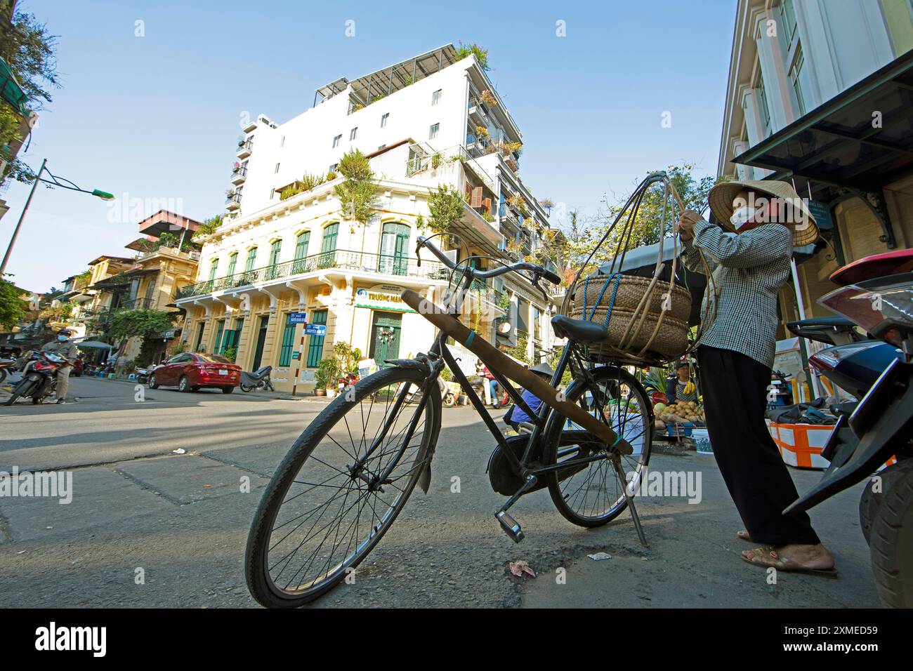 Femme vietnamienne avec chapeau conique prépare son vélo pour sa tournée de vente à travers le vieux quartier, perspective grenouille, Hanoi, Vietnam Banque D'Images