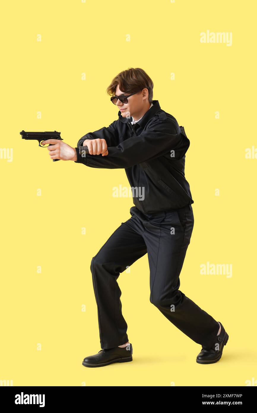Garde de sécurité masculin avec arme à feu et lampe de poche sur fond jaune Banque D'Images