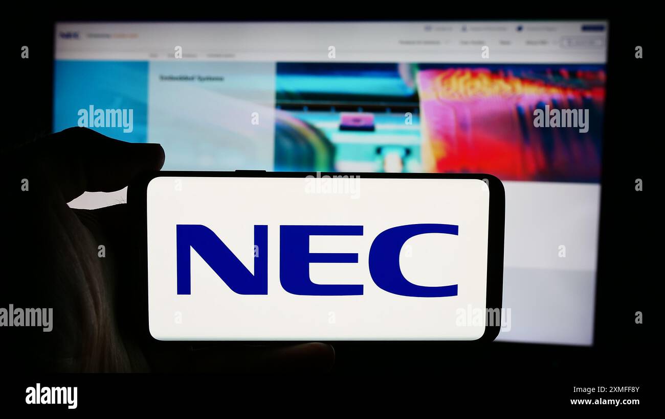 Personne tenant le téléphone portable avec le logo de la société japonaise de technologie de l'information NEC Corporation en face de la page Web. Concentrez-vous sur l'affichage du téléphone. Banque D'Images