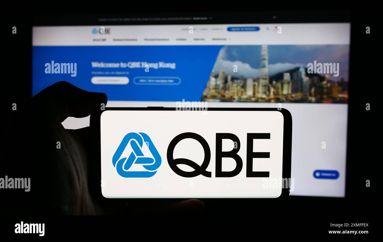 Personne tenant le téléphone portable avec le logo de la société australienne QBE Insurance Group Limited devant la page Web de l'entreprise. Concentrez-vous sur l'affichage du téléphone. Banque D'Images