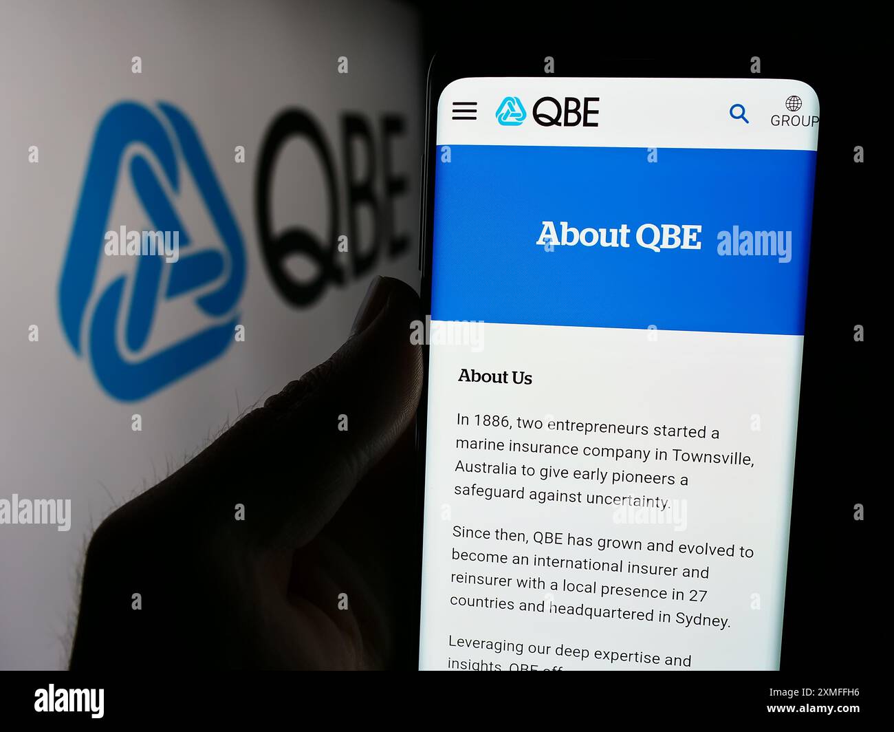 Personne tenant le téléphone portable avec la page Web de la société australienne QBE Insurance Group Limited devant le logo. Concentrez-vous sur le centre de l'écran du téléphone. Banque D'Images