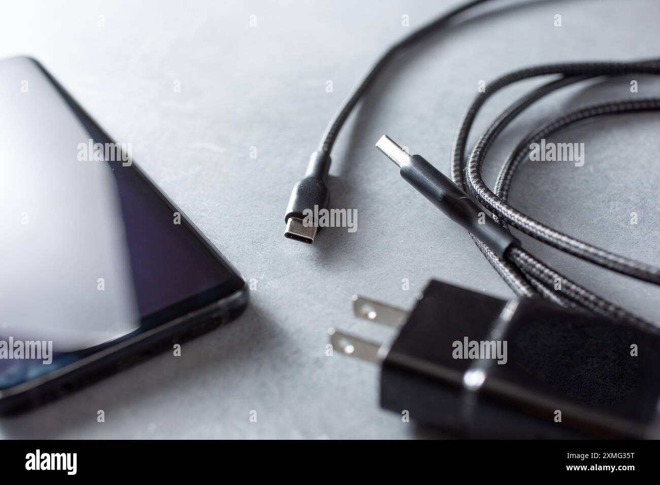 Vue rapprochée d'un cordon d'alimentation et d'une fiche à côté d'un téléphone cellulaire. Banque D'Images