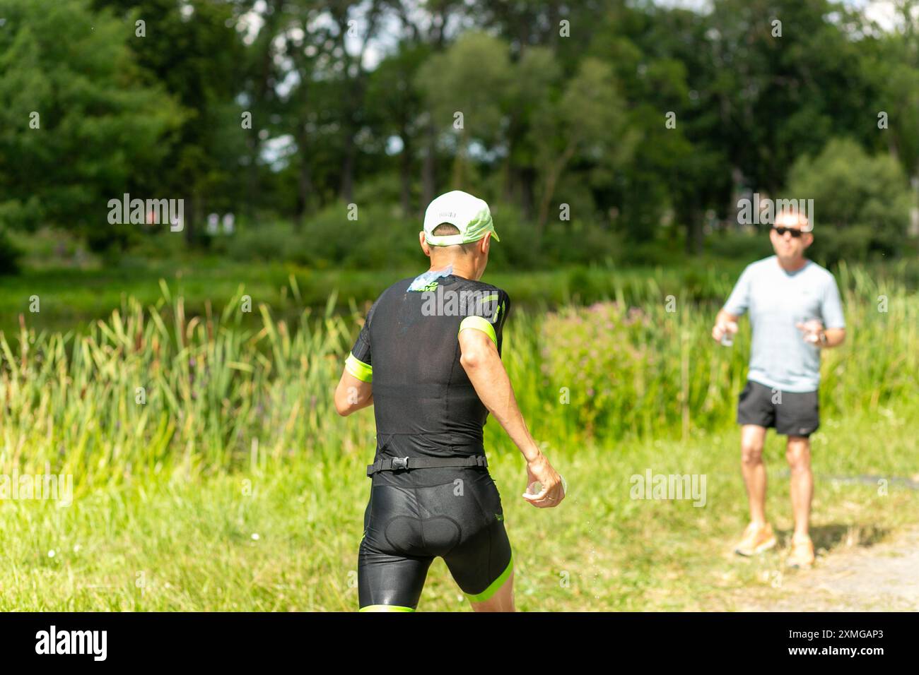 Un volontaire tient une tasse d'eau en plastique à un coureur de triathlon. L'image capture l'esprit de soutien et de communauté lors d'un événement sportif, souligne Banque D'Images