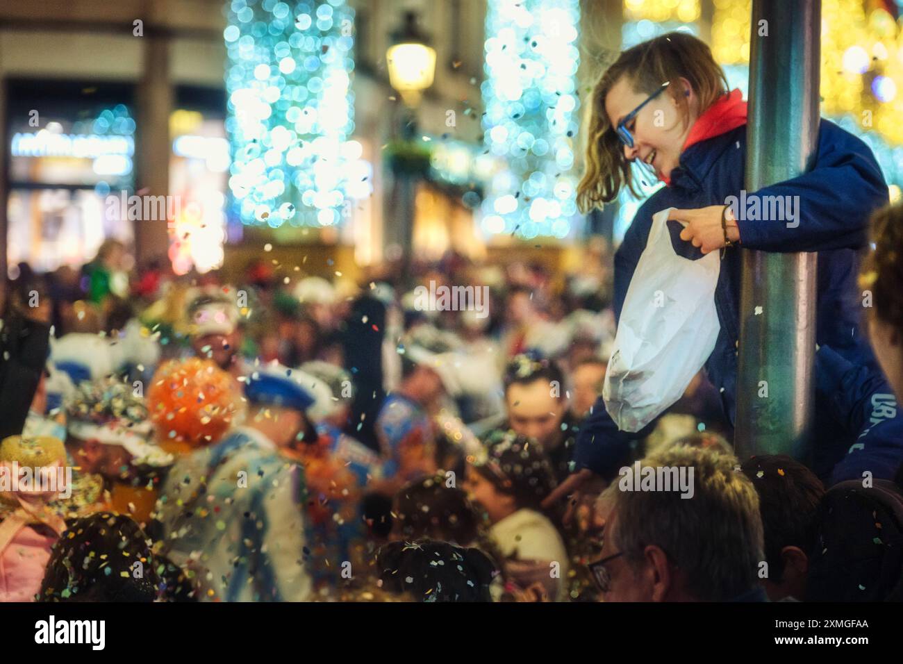 Enfant curieux avec des lunettes observant l'événement festif de foule, captivé par des confettis ou des flocons de neige dansant dans l'air. Capture le pur plaisir et l'émerveillement. Banque D'Images