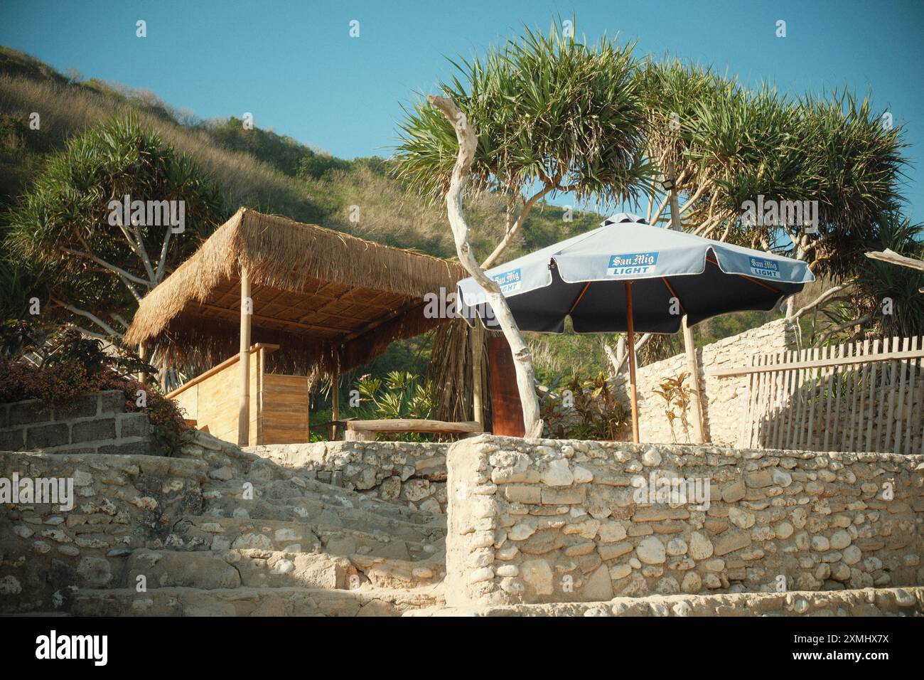 Pecatu, Bali, Indonésie - 15 juillet 2024 : un stand de nourriture, de collation et de boisson sur la plage avec des tables de pique-nique parasol sur une île tropicale et vert hil Banque D'Images