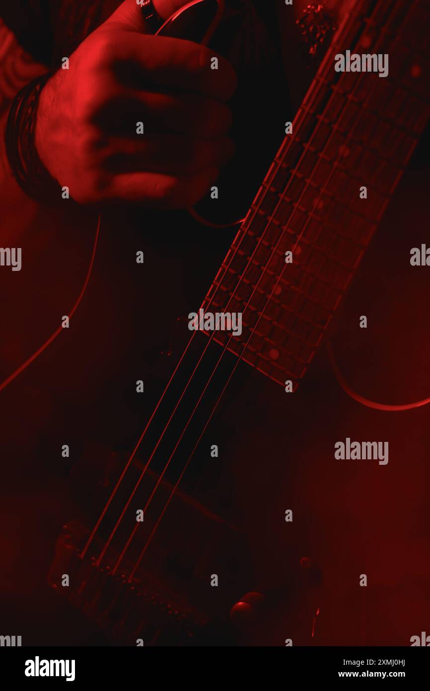 Un gros plan détaillé de la main d'un guitariste électrique saisissant une guitare, illuminé par un éclairage rouge, mettant en valeur l'instrument et le style du musicien Banque D'Images