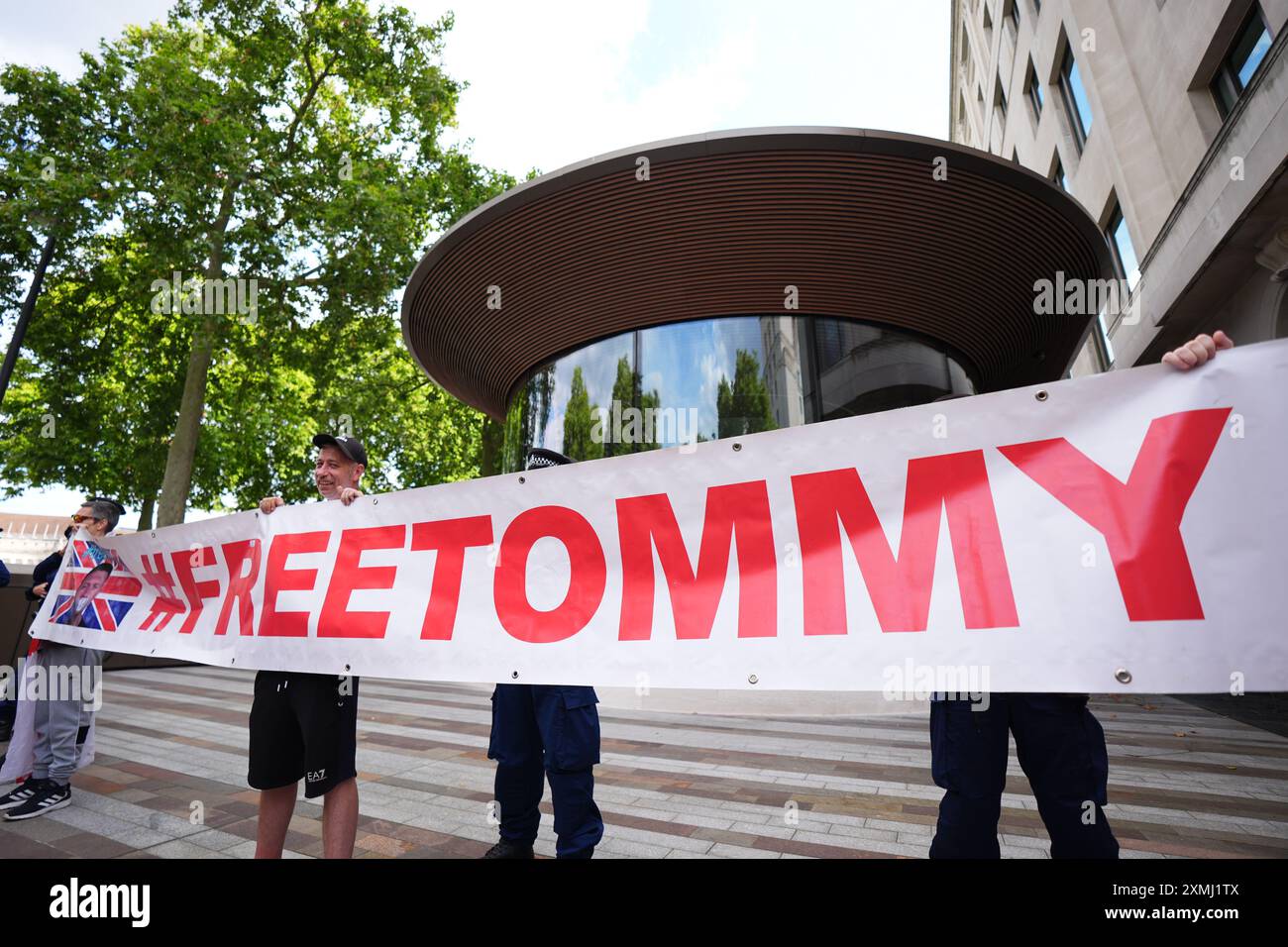 Des manifestants à l'extérieur de New Scotland Yard à Londres protestent contre l'arrestation présumée de Tommy Robinson. Tommy Robinson a été arrêté en vertu des lois anti-terroristes, selon son compte X vérifié. Sa détention fait suite à une plainte concernant un film qui aurait été montré à la foule lors d'une marche dans le centre de Londres samedi dirigée par M. Robinson, de son vrai nom Stephen Yaxley Lennon. Date de la photo : dimanche 28 juillet 2024. Banque D'Images