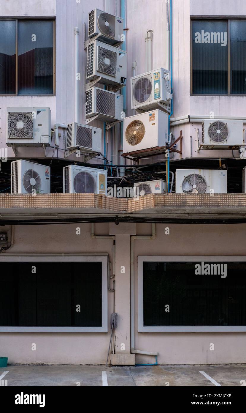 De nombreuses unités de fenêtres AC empilées de manière désordonnée sur la façade d'un bâtiment à Bangkok, en Thaïlande. Banque D'Images