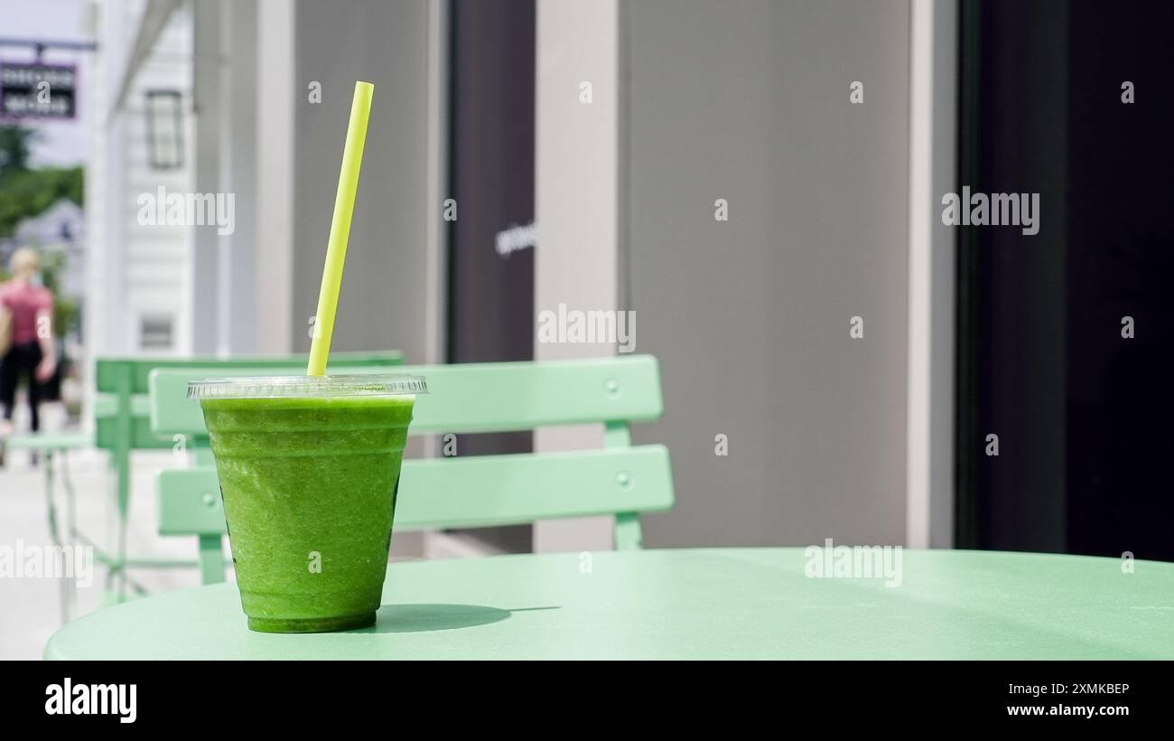Un smoothie vert éclatant se trouve sur une table vert pastel à l'extérieur d'un café. Est entouré par une atmosphère détendue, avec des gens marchant tranquillement dans le dos Banque D'Images