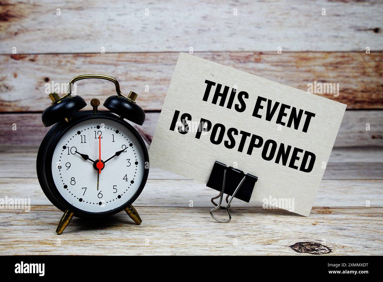 Cet événement est reporté texte sur carte papier avec réveil sur fond en bois Banque D'Images