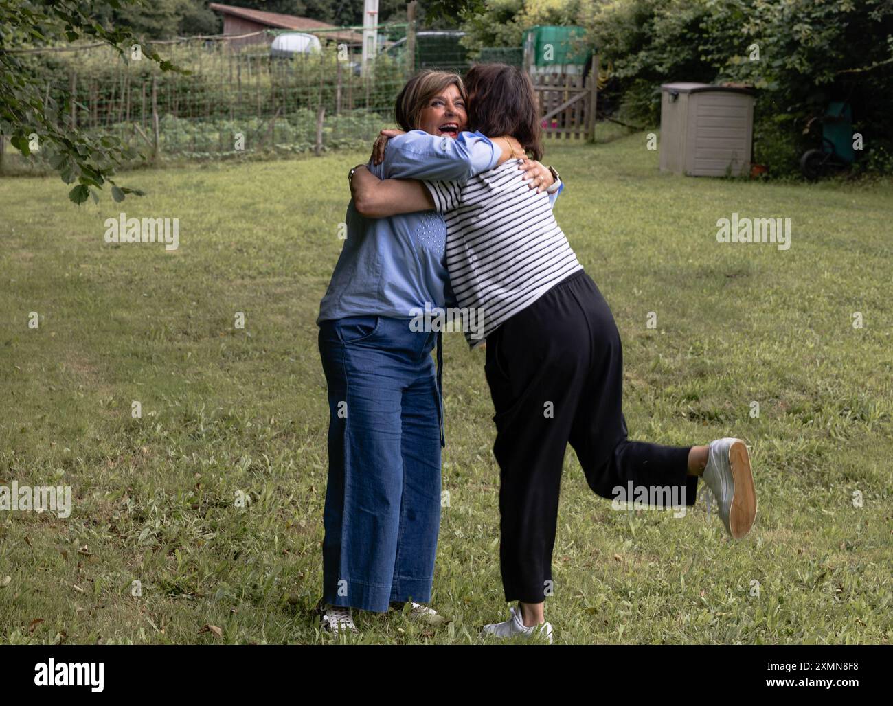 Deux amis partagent une étreinte chaleureuse à leur arrivée à un pique-nique à la campagne, célébrant leur amitié dans un champ verdoyant. Banque D'Images