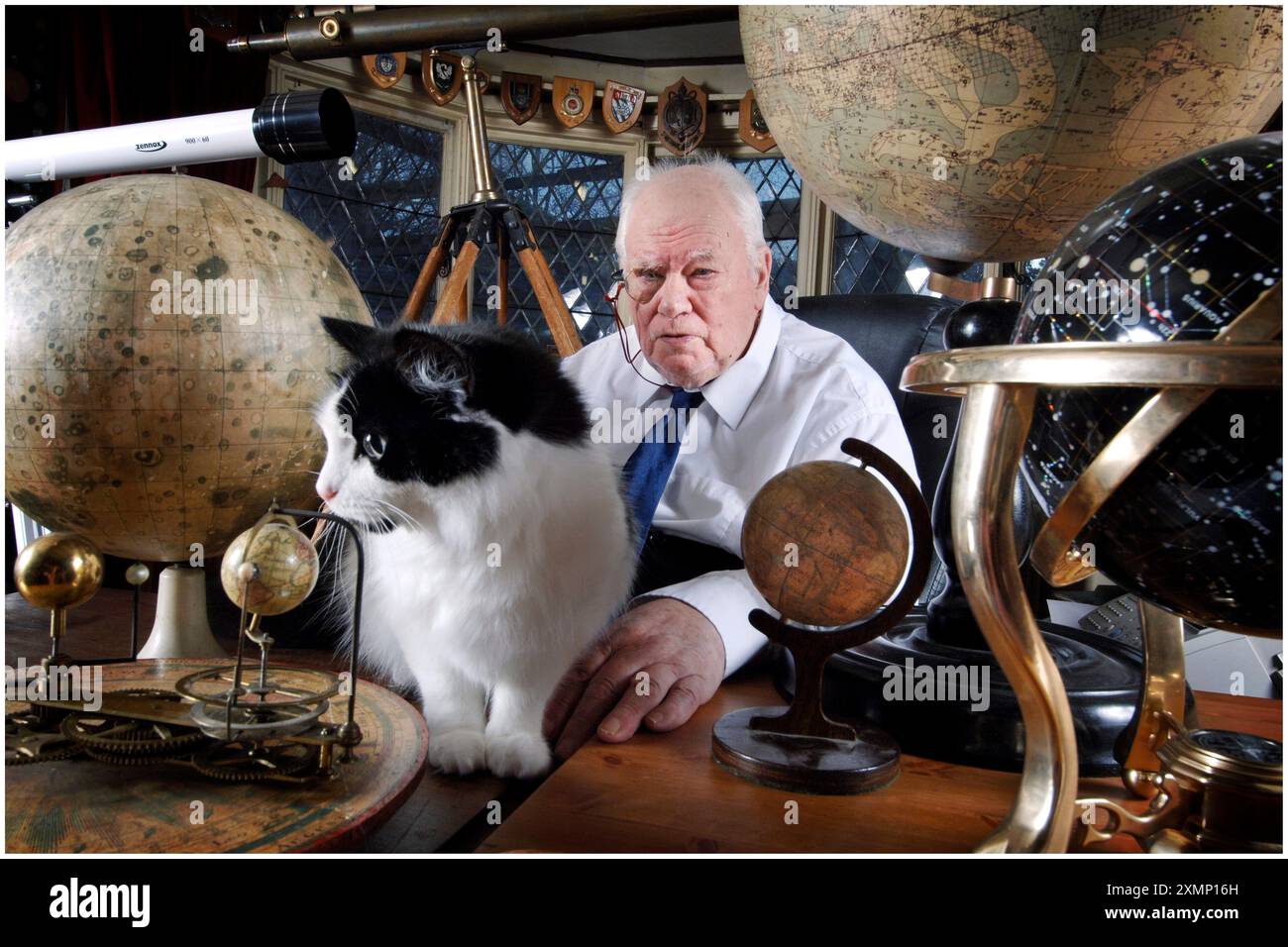 Photo de Roger Bamber : 18 décembre 2006 : L'astronome Sir Patrick Moore, présentateur de 'The Sky at Night' pendant 50 ans, se détend dans son étude à Selsey, West Sussex, lors d'une pause dans le tournage, entouré de globes de planète, télescopes et d'un de ses deux chats Jeannie. Le spectacle enregistrait son 650e spectacle à la maison. Banque D'Images Photo de Roger Bamber : 18 décembre 2006 : L'astronome Sir Patrick Moore, présentateur de 'The Sky at Night' pendant 50 ans, se détend dans son étude à Selsey, West Sussex, lors d'une pause dans le tournage, entouré de globes de planète, télescopes et d'un de ses deux chats Jeannie. Le spectacle enregistrait son 650e spectacle à la maison. Banque D'Images