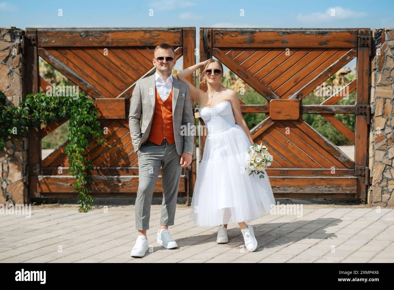 jeune couple mariée dans une robe courte blanche et marié dans un costume gris près de la porte rurale en bois de la propriété Banque D'Images
