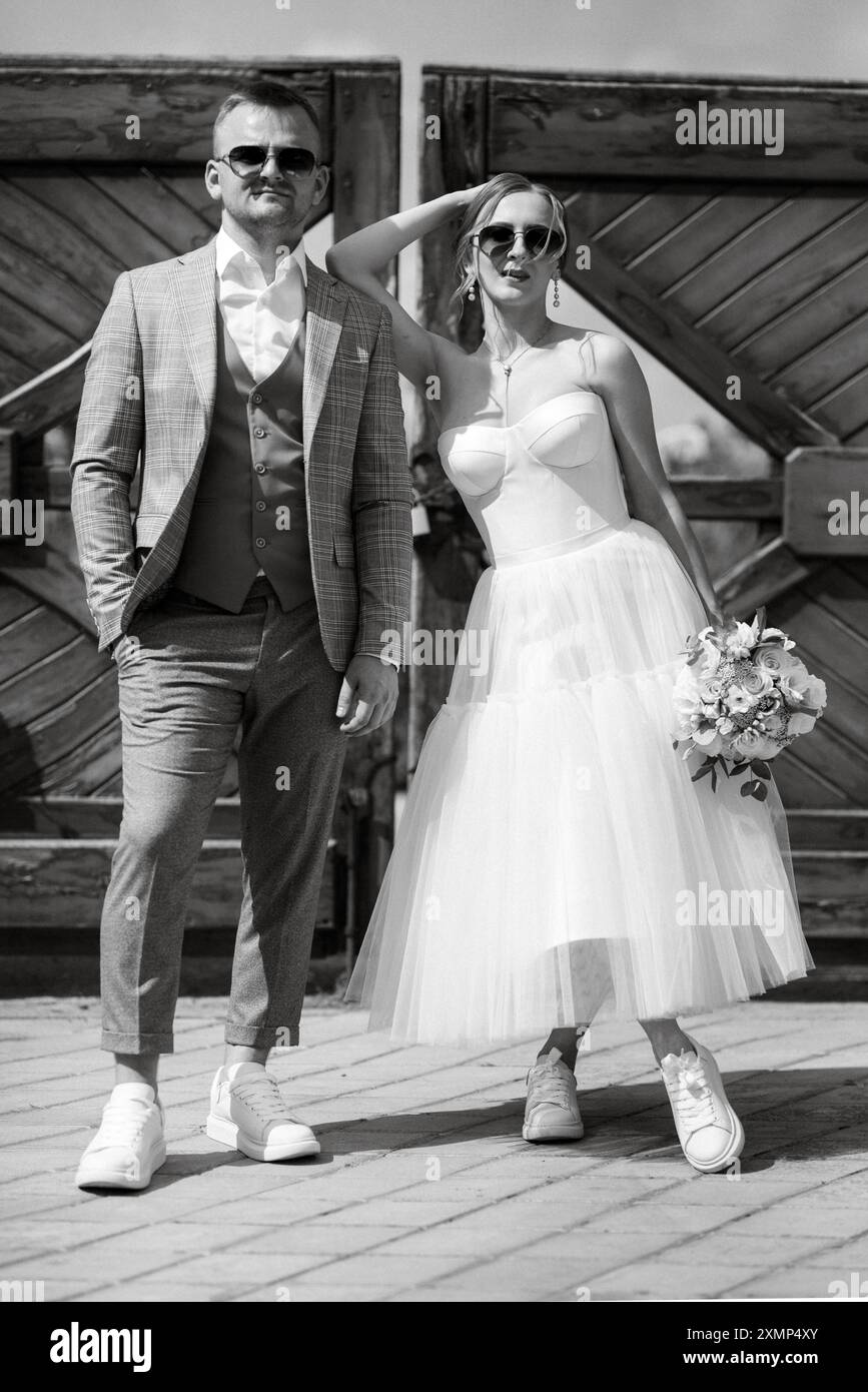 jeune couple mariée dans une robe courte blanche et marié dans un costume gris près de la porte rurale en bois de la propriété Banque D'Images