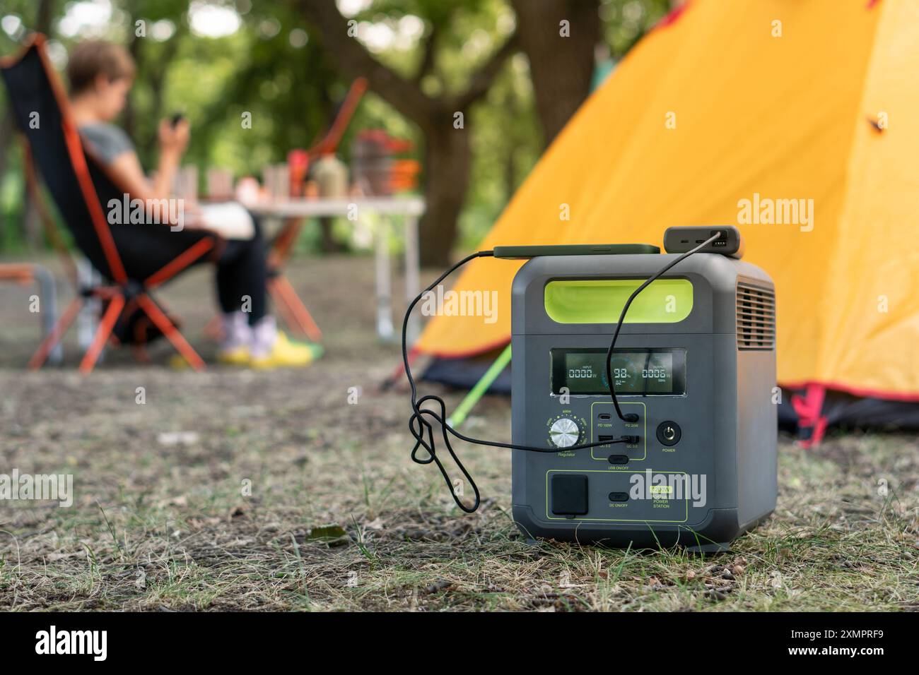 Centrale électrique portable avec batterie de ferrophosphate de lithium chargant des dispositifs électroniques utilisés sur un site de camp sauvage, devant une tente jaune. Portable Banque D'Images