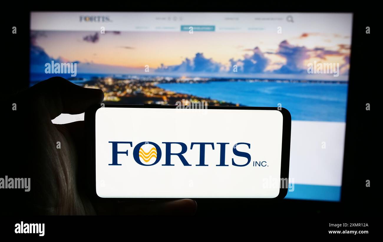 Personne tenant un téléphone cellulaire avec le logo de la compagnie canadienne de services publics d'électricité Fortis Inc. devant la page Web de l'entreprise. Concentrez-vous sur l'affichage du téléphone. Banque D'Images