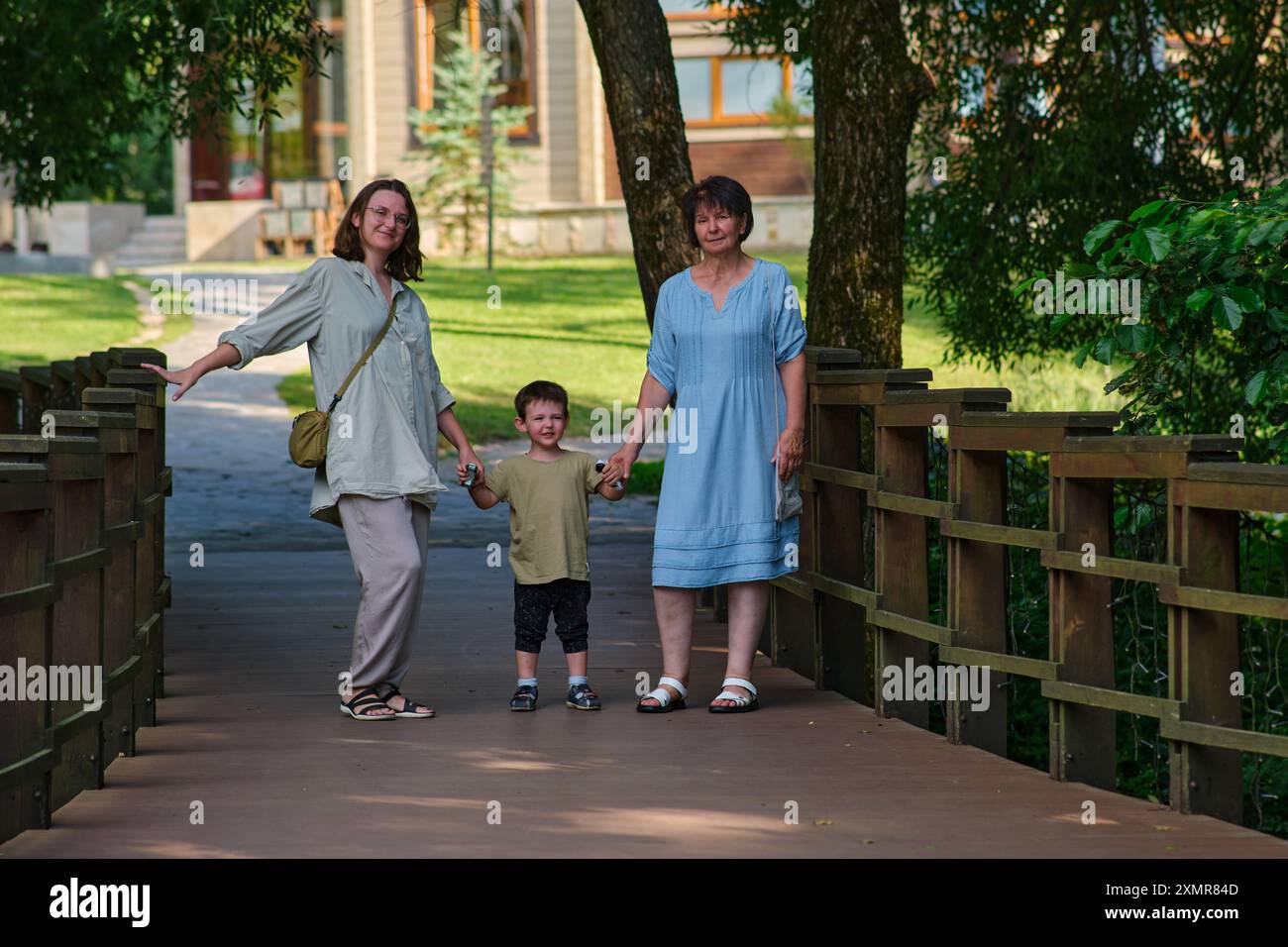 Trois générations de famille, dont une femme âgée, une femme adulte et un enfant, debout sur un pont en bois dans un parc. Portrait extérieur pour le design et Banque D'Images