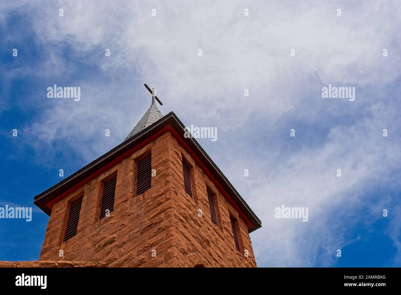 Tour de l'église en grès rouge de St Joseph surmontée de crucifix contre le ciel sombre Banque D'Images