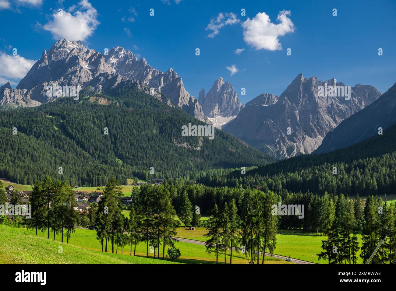 Sexten, Italie les sommets imposants des Dolomites s'élèvent majestueusement contre un ciel bleu éclatant, parsemé de nuages moelleux. Vallées verdoyantes et denses fo Banque D'Images