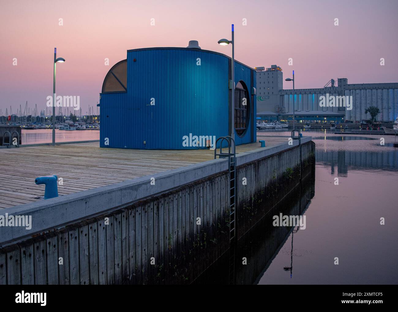 Québec, Canada - 18 juillet 2023 : un petit bâtiment bleu dans le vieux port de Québec au crépuscule avec un peu d'éclairage et quelques personnes méconnaissables dedans Banque D'Images