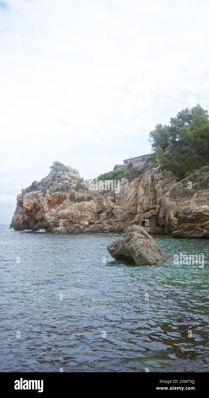 La plage pittoresque de cala deia à majorque présente des falaises escarpées, des eaux turquoises sereines et une végétation luxuriante par temps couvert. Banque D'Images