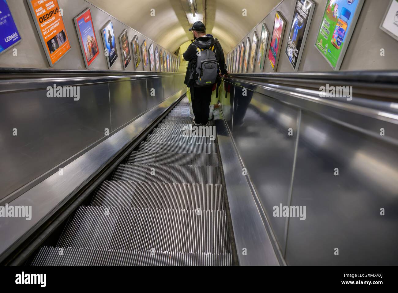 Un homme avec un sac à dos sur un escalator descendant vers une ligne de métro londonienne, vide, argenté, isolé Banque D'Images