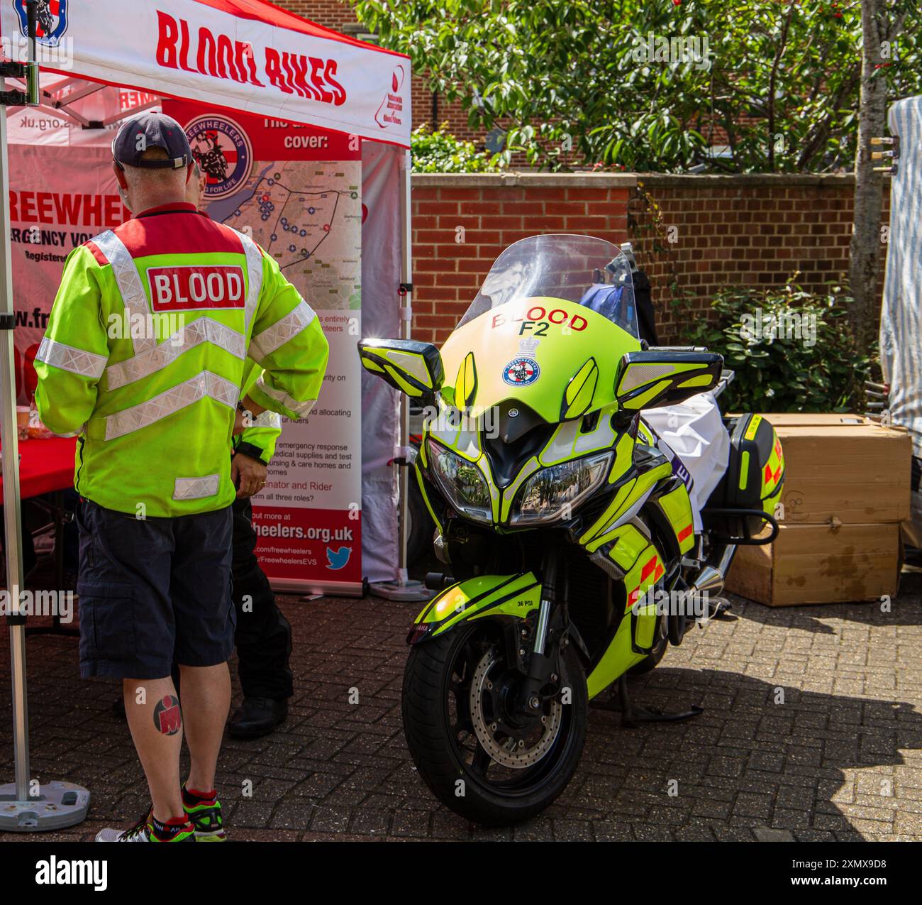 Bénévole à un stand Blood Bikes à côté d'une moto, soulignant les services médicaux d'urgence caritatifs fournis. Banque D'Images