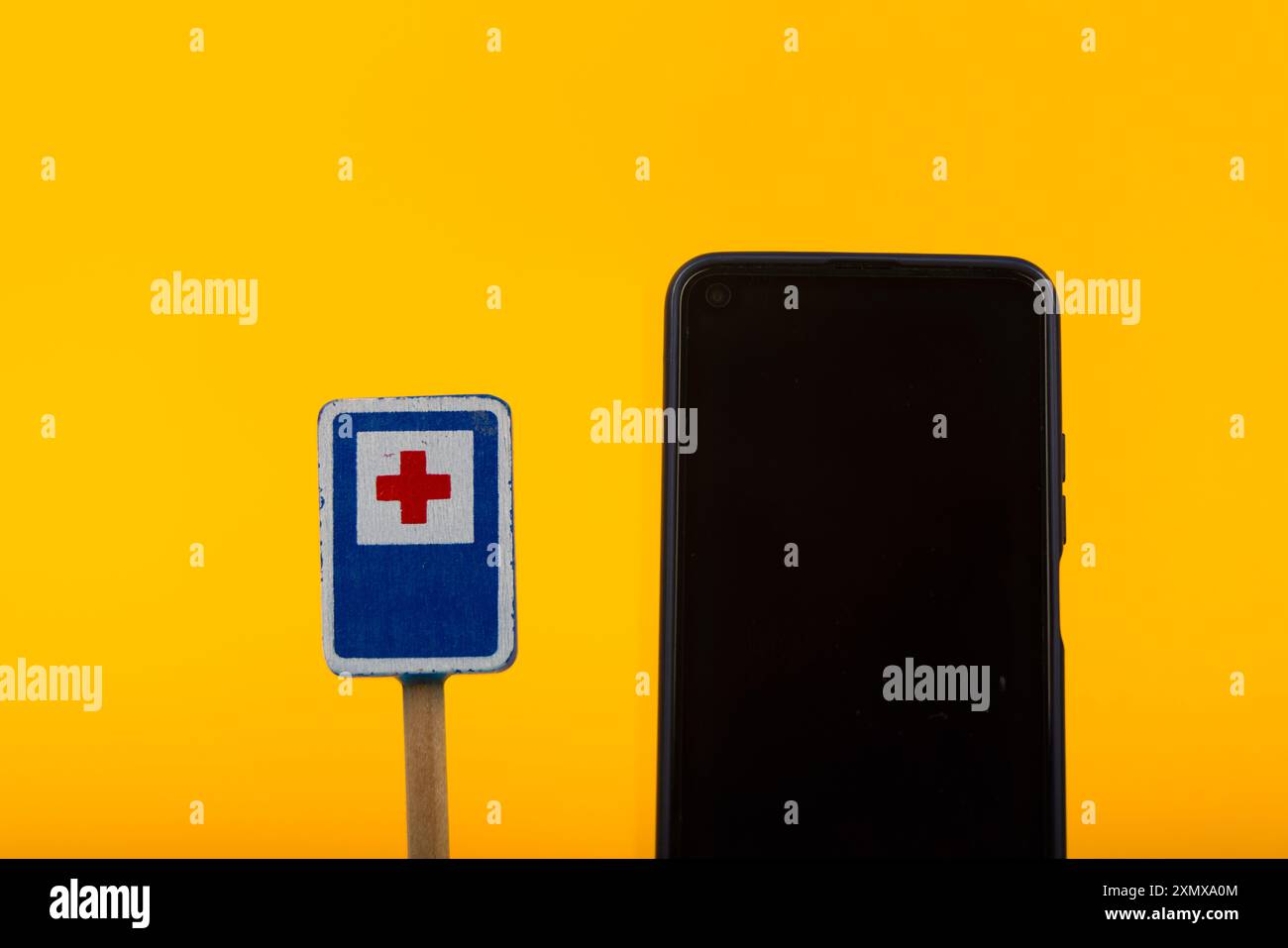 Un panneau d’avertissement hospitalier en bois associé à un smartphone sur fond jaune, soulignant le contraste entre les anciens et les nouveaux outils de communication Banque D'Images