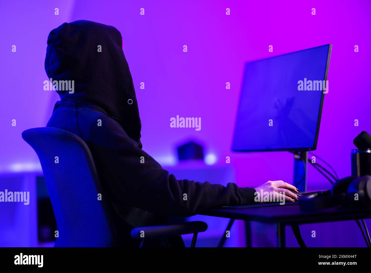 Joueur professionnel en hoody jouant au jeu vidéo dans une pièce colorée avec une configuration moderne Banque D'Images