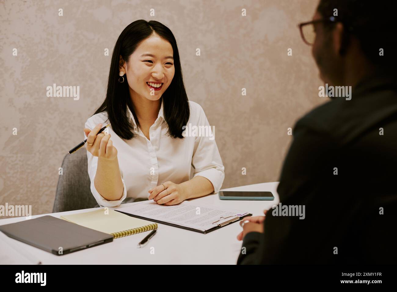 Sympathique jeune responsable des ressources humaines asiatique souriant lors d'un entretien avec un candidat noir méconnaissable, au-dessus de l'épaule Banque D'Images