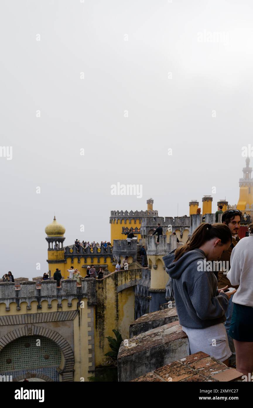 Visiteur regardant son téléphone tout en explorant les tours jaunes vibrantes et les remparts du palais de Pena par une journée brumeuse Banque D'Images