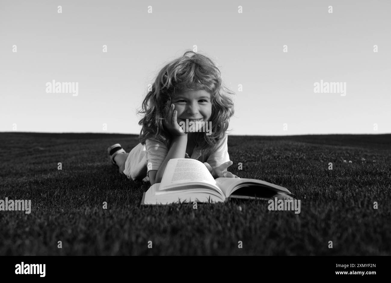Un petit garçon qui lit un livre dans un parc à l'extérieur.Sourire drôle d'enfant dans le t-shirt avoir plaisir lecture livre dans le parc. Banque D'Images