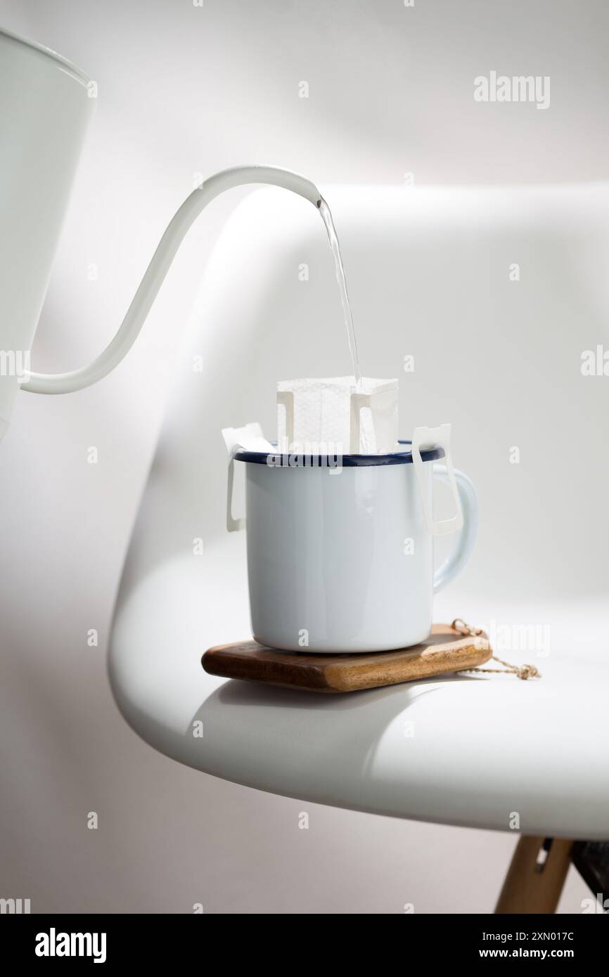 Cette photographie illustre le processus d'égouttement de l'eau chaude à travers un sac de café pré-fait dans une tasse en céramique blanche avec des bords bleu foncé, placé Banque D'Images