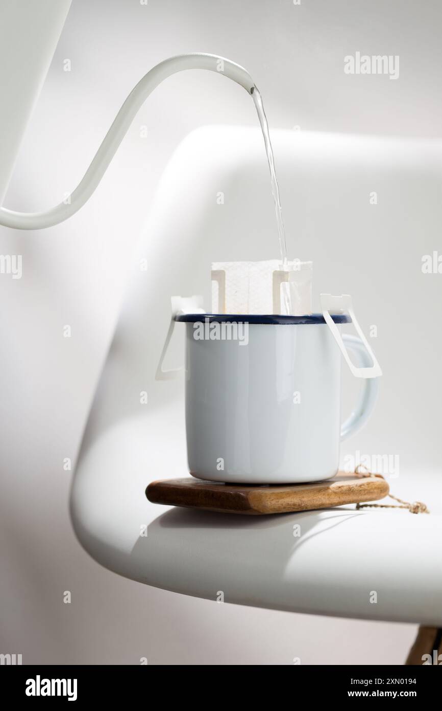 Cette photographie illustre le processus d'égouttement de l'eau chaude à travers un sac de café pré-fait dans une tasse en céramique blanche avec des bords bleu foncé, placé Banque D'Images