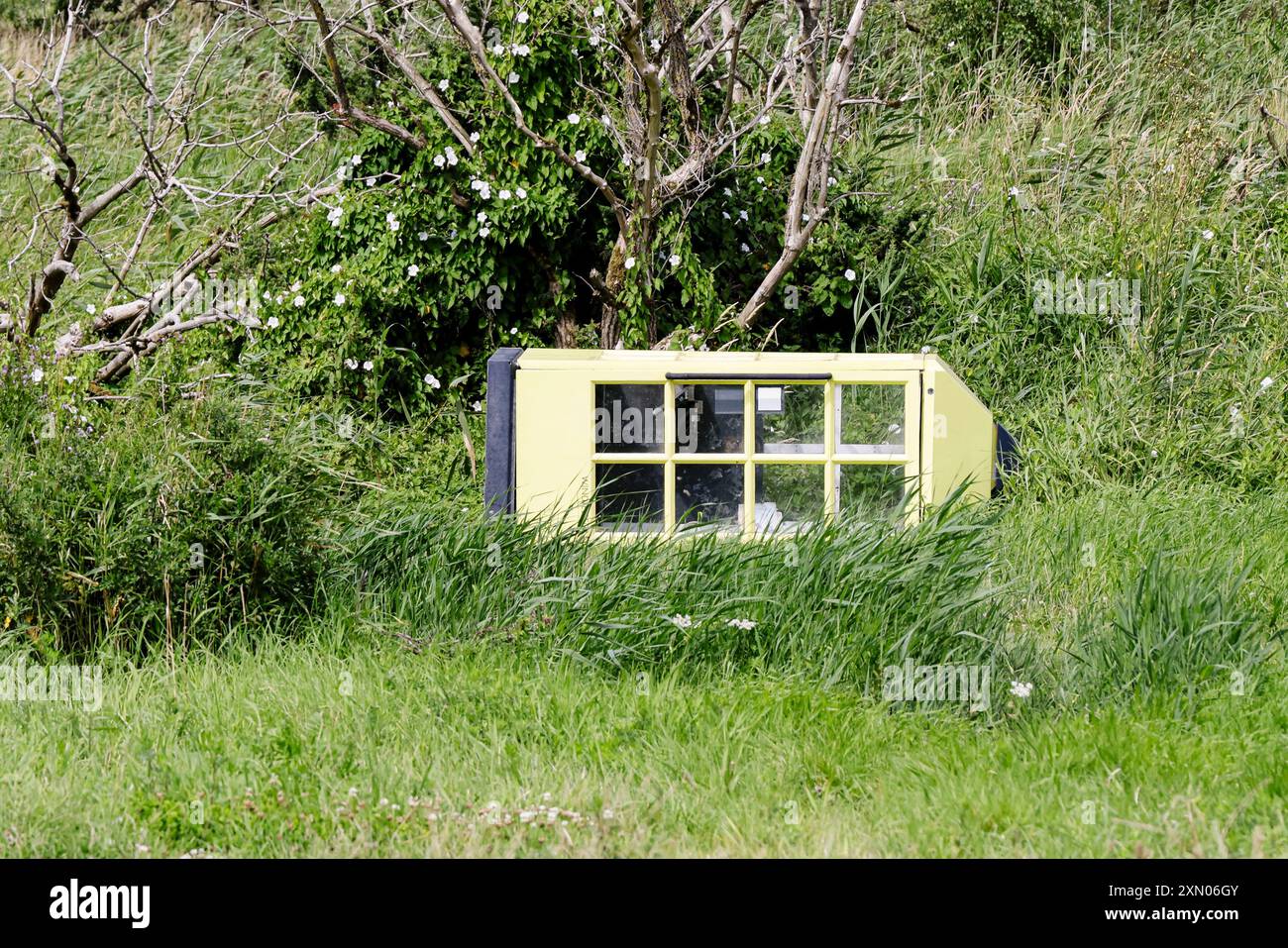 Arnis, Allemagne. 24 juillet 2024. Une vieille cabine téléphonique se trouve sur les rives du Schlei, inondé lors de la grave onde de tempête de la mer Baltique à l'automne 2023. La digue à Arnis a été percée sur une longueur de 60 mètres. Tout le long de la côte, des digues et des installations portuaires ont été endommagées ou détruites, et des maisons, des campings et des hôtels ont été dévastés. Le gouvernement de l'État a estimé les dégâts à environ 200 millions d'euros. Crédit : Frank Molter/dpa/Alamy Live News Banque D'Images