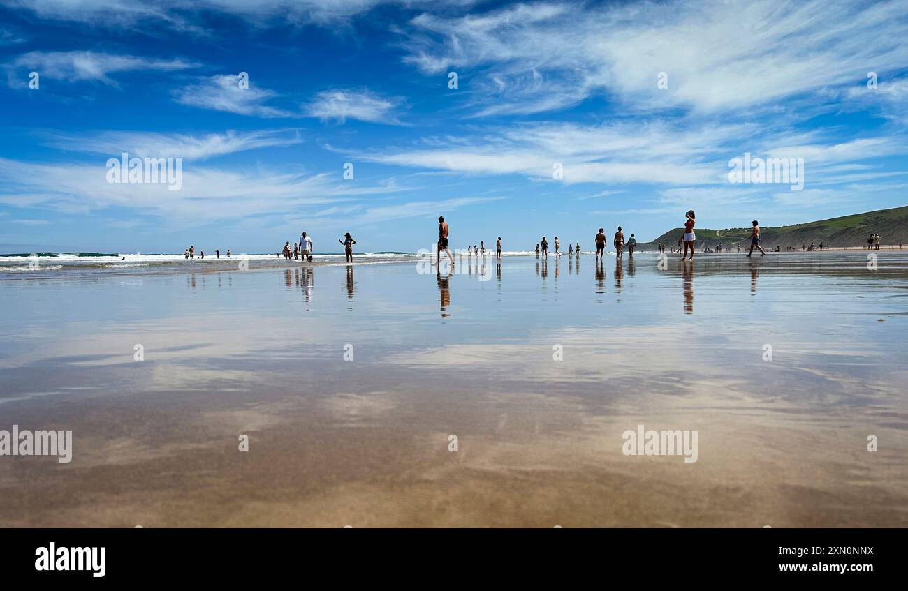 Vue panoramique sur la plage de Gerra, en Cantabrie. avec le ciel et quelques personnes marchant sur la plage et reflétant dans le sable humide. Banque D'Images