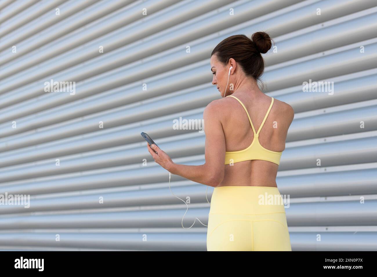 Vue arrière d'une femme sportive tenant un téléphone et portant des écouteurs tout en se préparant à l'exercice à l'extérieur Banque D'Images