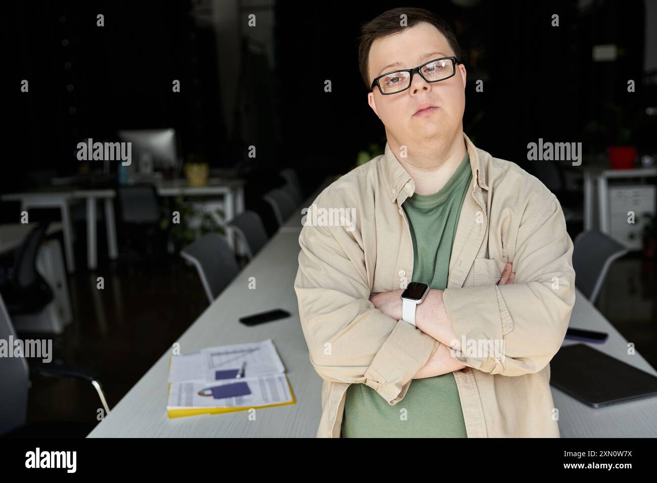 Un homme atteint du syndrome de Down se tient confiant dans un bureau avec les bras croisés. Banque D'Images