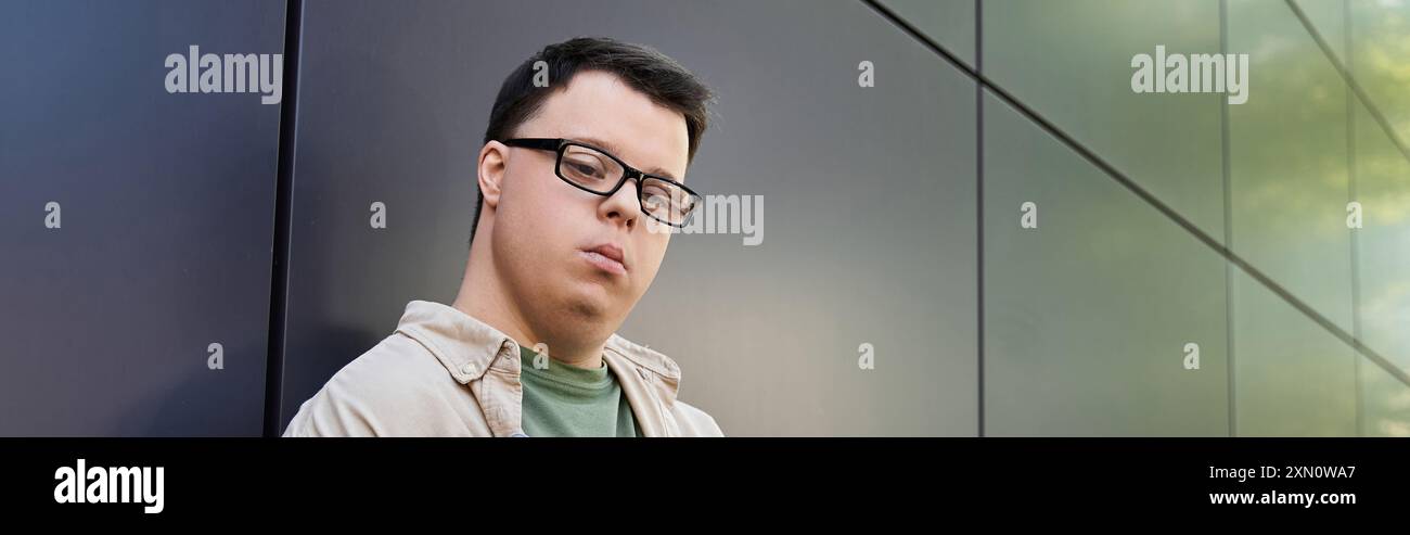 Un jeune homme atteint du syndrome de Down se tient dehors, appuyé contre un mur. Banque D'Images