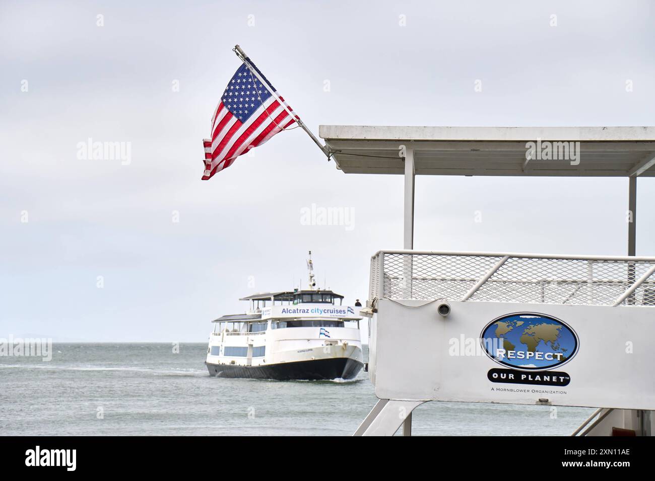San Francisco, Californie, États-Unis d'Amérique - 14 juin 2024 : un ferry Alcatraz City Cruises approche de San Francisco tandis qu'un drapeau américain flotte au premier plan *** Eine Fähre der Alcatraz City Cruises nähert sich San Francisco, während eine amerikanische Flagge im Vordergrund weht Banque D'Images