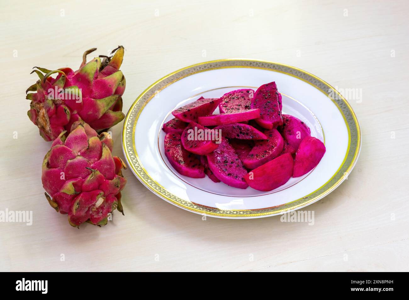 Délicieuses tranches de fruits de dragon sur une assiette blanche sur fond en bois. Deux fruits de dragon entiers placés à côté de l'assiette. Banque D'Images