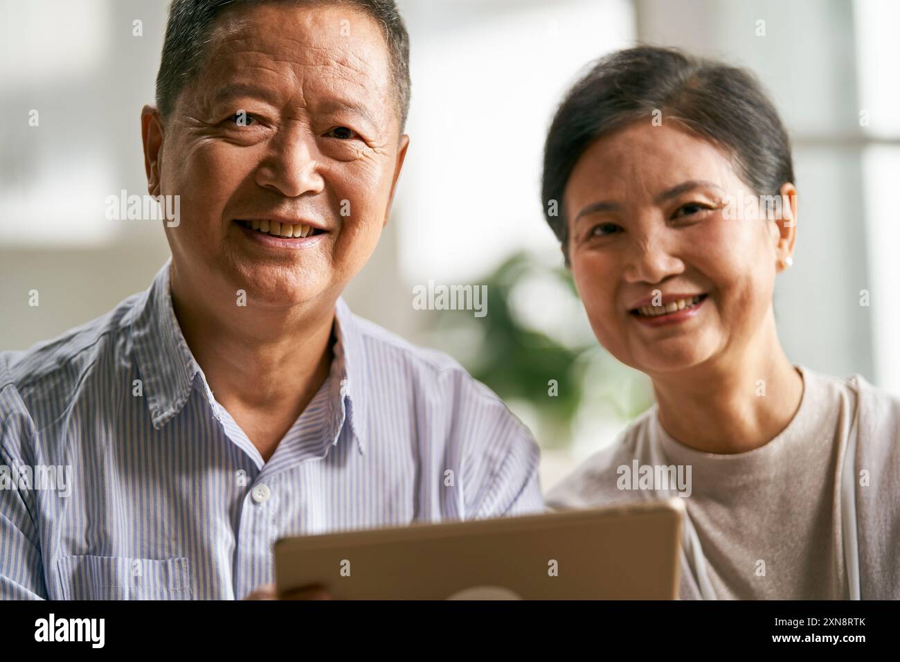 heureux couple asiatique senior assis sur le canapé à la maison en utilisant la tablette numérique ensemble Banque D'Images