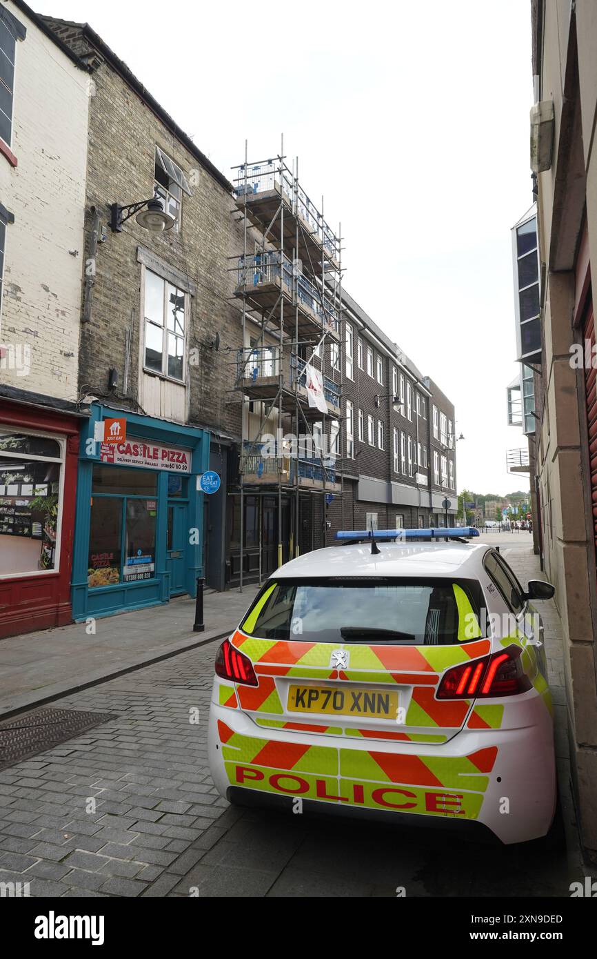 Une voiture de police garée devant un bâtiment désaffecté (centre gauche) à Fore Bondgate, Bishop Auckland dans le comté de Durham, après qu'un squelette de bébé ait été trouvé sous les planches du plancher par des entrepreneurs travaillant à la rénovation d'une propriété. Date de la photo : mercredi 31 juillet 2024. Banque D'Images