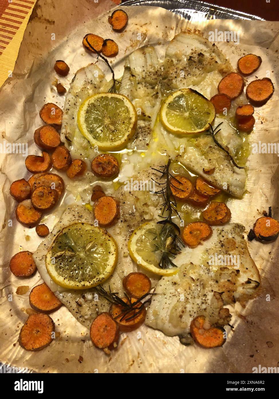 Pose verticale à plat de poisson blanc cuit avec des carottes, du citron et du romarin. Banque D'Images