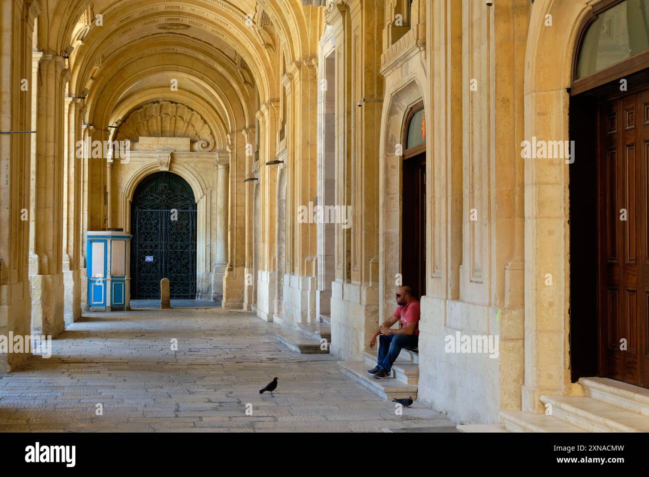 Un homme avec son sandwich et deux pigeons affamés dans l'arcade de la Bibliothèque nationale - la Valette, Malte Banque D'Images