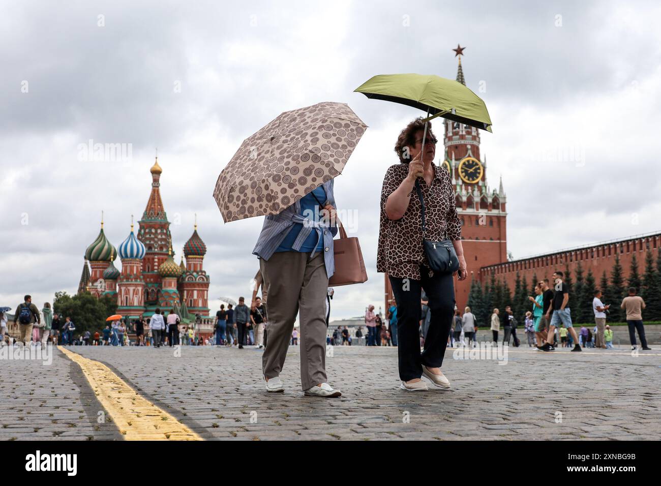 Femmes avec des parapluies marchant sur la place Rouge sur fond de la cathédrale de Basile. Pluie en ville en été Banque D'Images